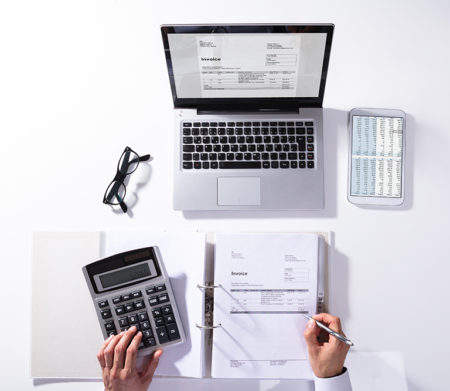 High Angle View Of Businessperson Calculating Invoice With Laptop On Desk