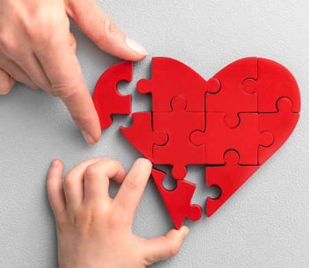 The concept of charity, love, donate and helping hand. International cardiology day. A woman and child arranges red heart shape puzzles. Symbol of helping others.